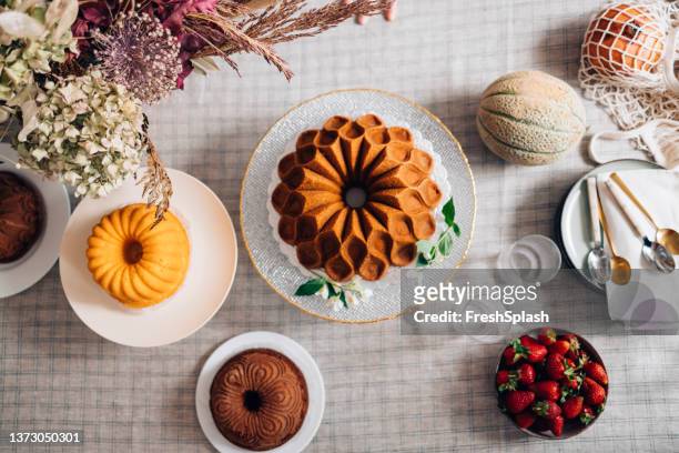 tasty bundt and angel cake on a white table cloth with plates and spoons - tulbandcake stockfoto's en -beelden