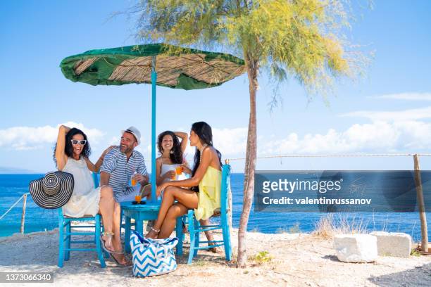 group of multiracial friends drinking cocktails at the seaside under a sun umbrella - drink umbrella stock pictures, royalty-free photos & images