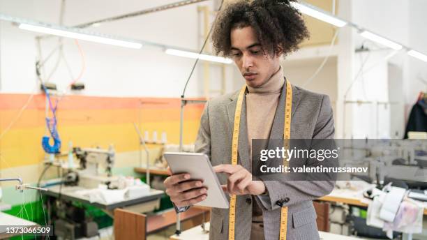 portrait of young african american professional fashion designer, with tape measure on his neck, standing in his  workplace and working on his digital tablet. - measuring success stock pictures, royalty-free photos & images