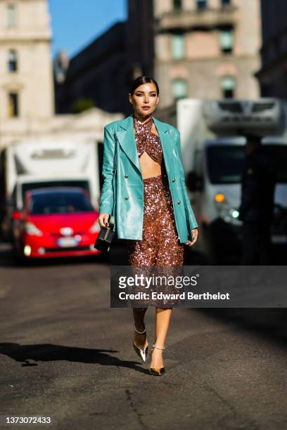 Karina Nigay wears a blue shiny leather blazer jacket, a brown sequined crossed neck / cropped top, a matching brown shiny embroidered sequined high...