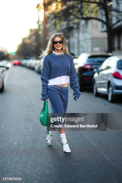 Emili Sindlev wears black sunglasses, a silver earrings, a white shirt, a blue braided wool cropped / backless pullover from Miu Miu, a matching blue...