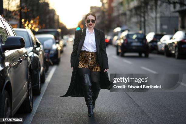 Merve Gorgoz wears black sunglasses, gold and pearls pendant earrings, white shirt, a black long blazer coat, a shoulder bag, brown and black leopard...