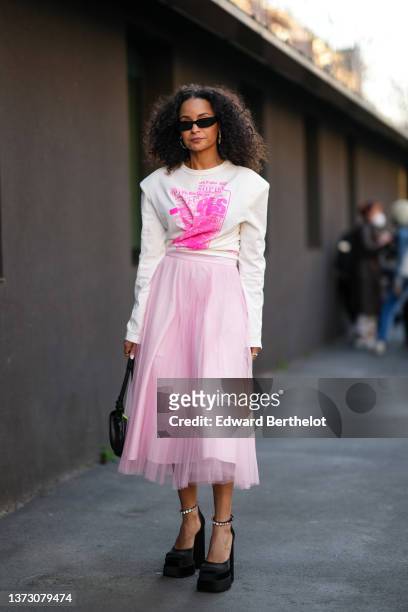 Sai De Silva wears black sunglasses, multicolored pearls earrings, a white with neon pink print pattern long sleeves t-shirt, a pale pink tulle...
