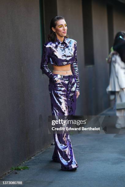 Ginevra Mavilla wears silver earrings, a purple sequined with blue and gold flower print pattern cropped shirt, matching high waist purple sequined...