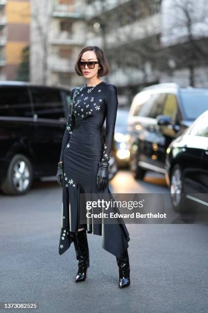 Chriselle Lim wears brown sunglasses, a black with yellow and white daisies print pattern long sleeves / asymmetric pleated midi dress, black shiny...