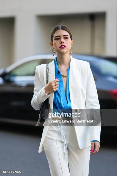 Guest wears gold Chiquito handbag pendant earrings from Jacquemus, a gold chain with black triangular pendant necklace from Prada, a black shiny...