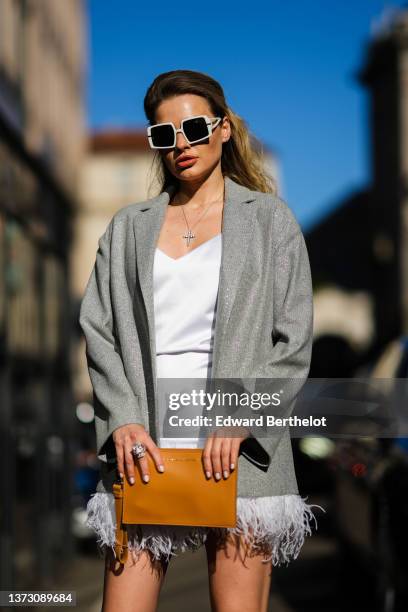 Guest wears white sunglasses, silver earrings, a silver with diamonds cross pendant necklace, a silver gray shiny blazer jacket, a white V-neck...