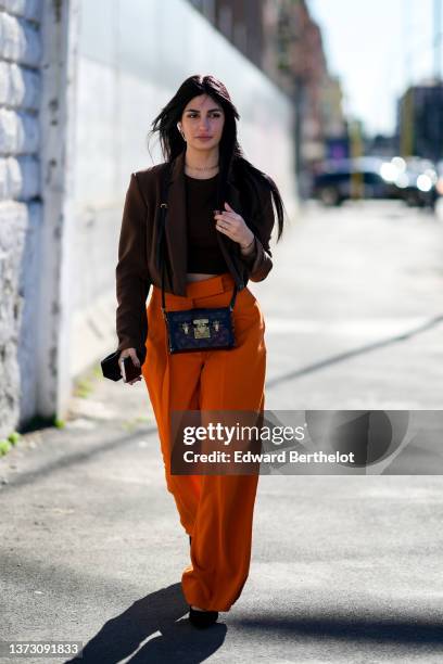 Guest wears gold earrings, a gold chain necklace from Dior, a dark brown cropped t-shirt, a dark brown cropped blazer jacket, a gold ring, high waist...