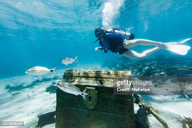 teenage girl scuba diving over a pirate chest on the bottom of the sea - schatkist stockfoto's en -beelden