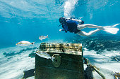 Teenage girl scuba diving over a pirate chest on the bottom of the sea