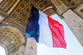 A large french flag fluttering under the Arc de Triomphe in Paris, France.