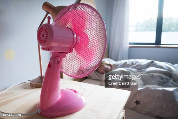 ピンクのファンが彼女の上に涼しい空気を吹いているベッドで眠っている女の子 - electric fan ストックフォトと画像