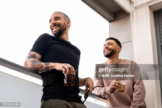 two male friends have a good time together while enjoying a cup of coffee or tea standing on a balcony. - bromance stock-fotos und bilder