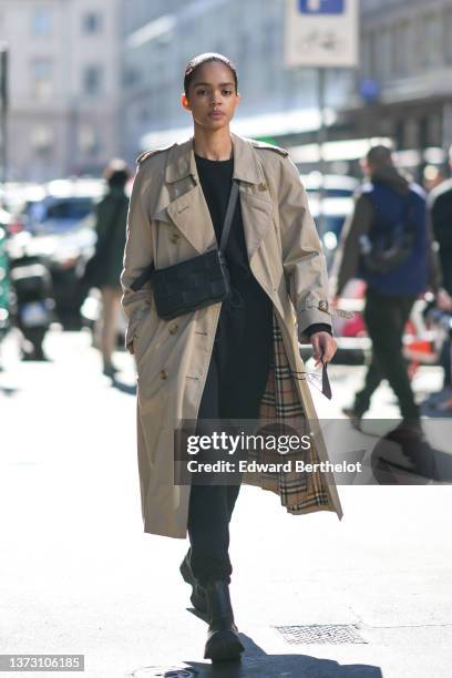 Guest wears a black sweater, black sport pants, a black shiny braided leather Cassette crossbody bag from Bottega Veneta, a beige long trench coat...