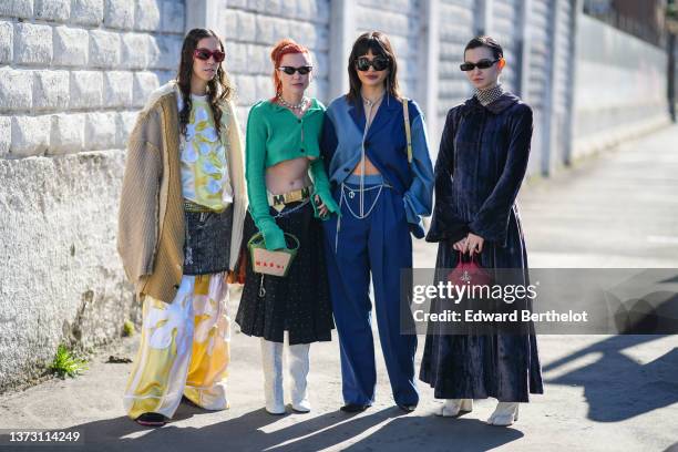 Guest wears red sunglasses, a white and gold embroidered print pattern silk oversized jumpsuit, a brown / camel / orange wool oversized cardigan, a...