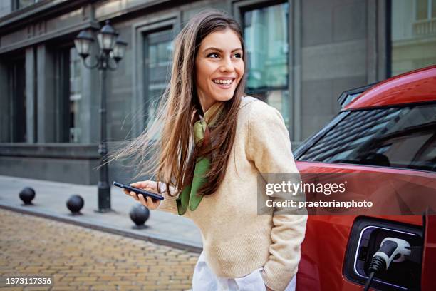 portrait of woman charging her electric car - smartphone car stock pictures, royalty-free photos & images