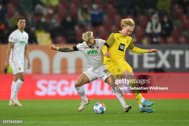 Niklas Dorsch of FC Augsburg challenges Julian Brandt of Borussia Dortmund during the Bundesliga match between FC Augsburg and Borussia Dortmund at...