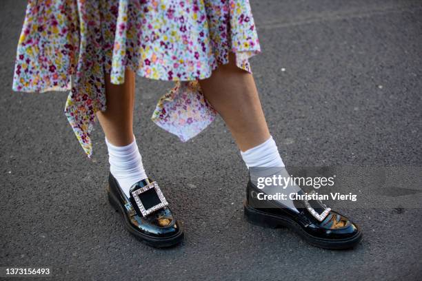 Candela Novembre is seen wearing black sunglasses, a white with yellow / purple / pink flower print pattern high neck / asymmetric midi dress, a...