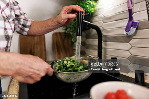 senior couple preparing a healthy vegetable salad at home. - running water faucet stock pictures, royalty-free photos & images