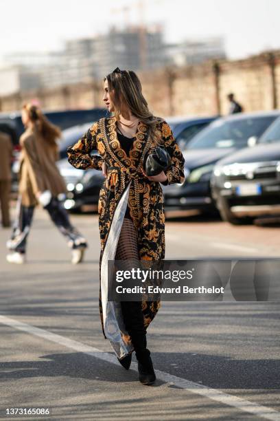 Guest wears black sunglasses, gold earrings, a gold chain necklace, a black V-neck short dress, a black and gold orange print pattern belted kimono...