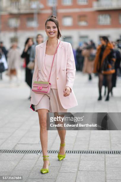 Gabrielle Caunesil wears a pale pink V-neck t-shirt, a pale pink blazer jacket, beige shiny leather shorts, a green / pink / yellow braided tweed...