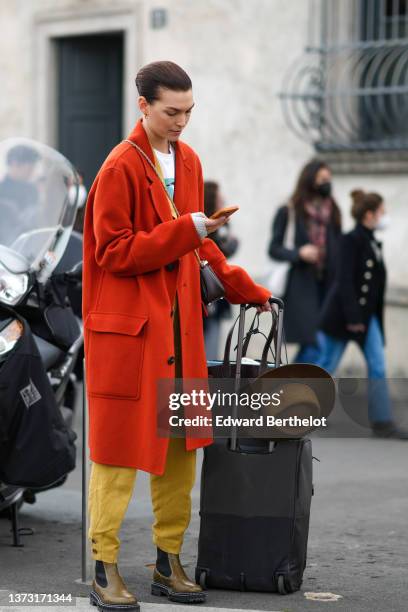 Guest wears an orange long coat, a white with multicolored print pattern t-shirt, yellow denim large jeans pants, a dark brown shiny leather...