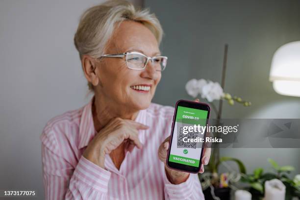 senior woman showing vaccination certificate on the phone - tonen stockfoto's en -beelden