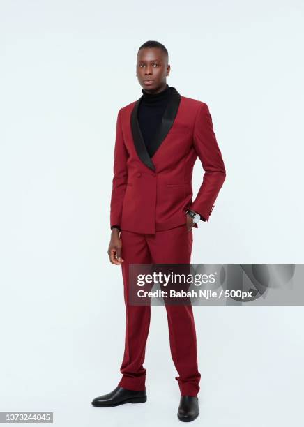 portrait of young man in red suit standing against white background,london,united kingdom,uk - red suit stockfoto's en -beelden