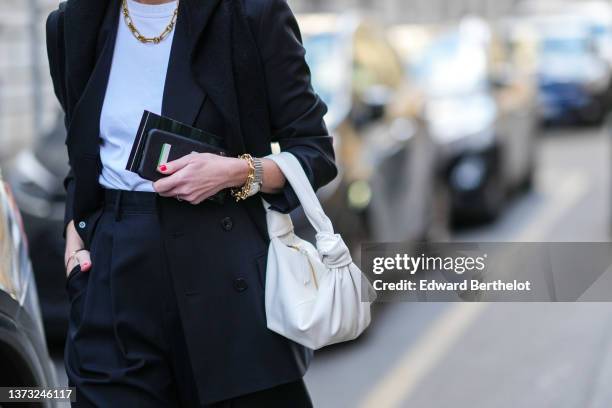 Guest wears a white t-shirt, a black blazer jacket, a gold large chain necklace, a white t-shirt, a gold chain bracelet, a gold watch, rings, high...