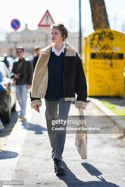 Model wears a white shirt, a black V-neck wool pullover, a dark brown leather with white sheep interior and collar aviator coat, pale gray suit...