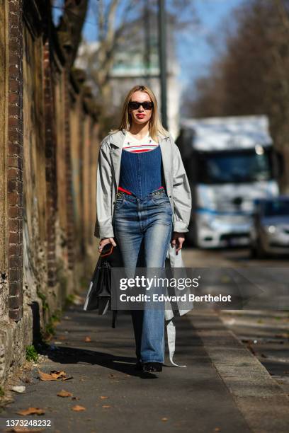 Guest wears black sunglasses, a white with red and green striped print pattern pullover, a navy blue denim corset, a pale gray oversized long coat,...