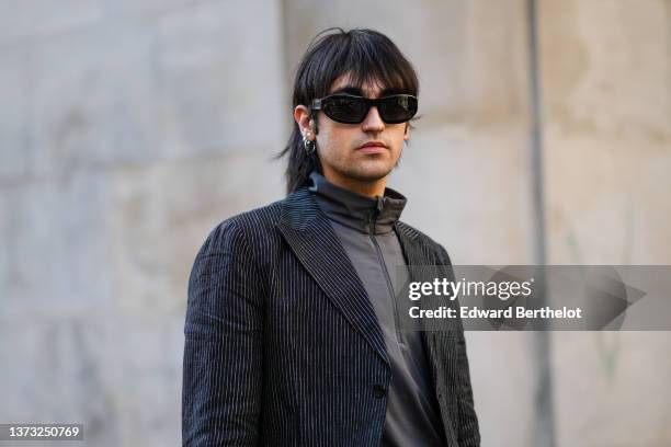 Guest wears black sunglasses, silver earrings, a dark gray zipper high neck t-shirt, a dark gray blazer jacket, outside the Armani fashion show,...
