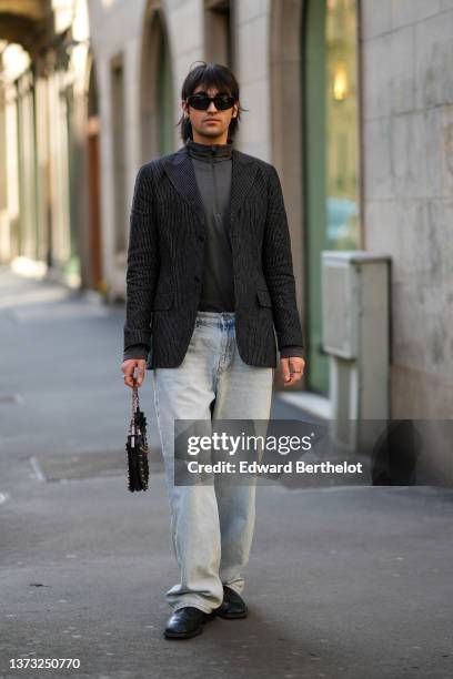 Guest wears black sunglasses, silver earrings, a dark gray zipper high neck t-shirt, a dark gray blazer jacket, blue faded denim jeans pants, a black...