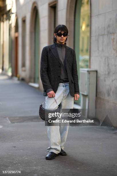 Guest wears black sunglasses, silver earrings, a dark gray zipper high neck t-shirt, a dark gray blazer jacket, blue faded denim jeans pants, a black...