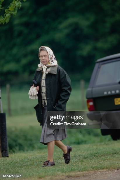 British Royal Queen Elizabeth II, wearing a green waxed jacket, grey skirt and a headscarf, attends the Royal Windsor Horse Show, held at Home Park...