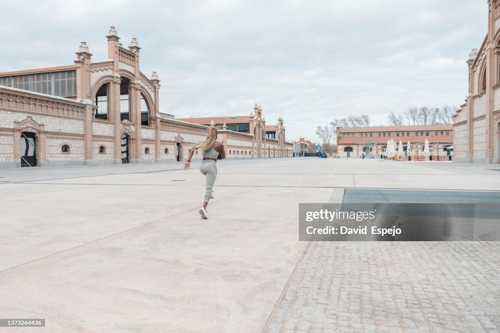 Anonymous ethnic female jogger training on city square