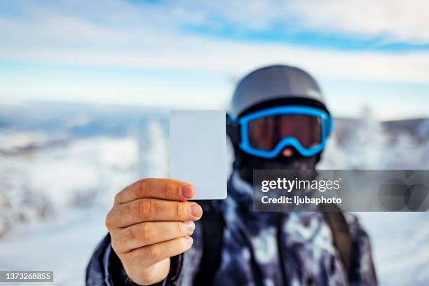 man with winter sport equipment looking at camerain  one hand  is showing a blank lift pass. - passes stockfoto's en -beelden