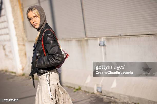 Guest poses ahead of the Marni fashion show wearing a black leather jacket, balaklava, beige long skirt and Marni printed bag during the Milan...