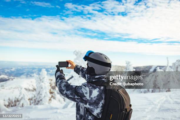 male skier takes a photo of nature, enjoying the winter snowy mountain landscape. - ski jacket stock pictures, royalty-free photos & images