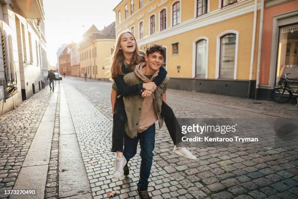 a teenage girl riding on the back of a boy friend - teen couple stock-fotos und bilder