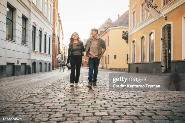 a teenage couple walking down a street holding hands - boys and girls town stockfoto's en -beelden