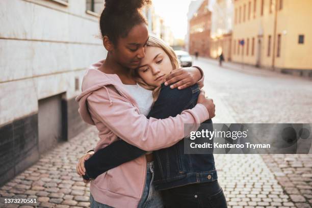 a teenage girl hugging her sad friend in city environment - grieving stock pictures, royalty-free photos & images