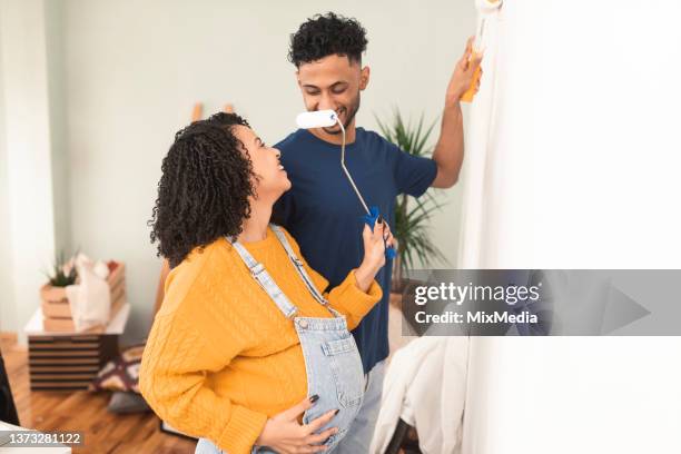 happy young couple expecting a baby and painting their new apartment - baby paint stock pictures, royalty-free photos & images