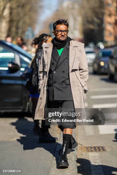 Guest wears glasses, a black scarf, a green sweater, a black blazer jacket, matching blazer suit shorts, a beige long coat, black high socks, black...