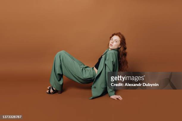 beautiful young woman model posing sitting in studio on a colored brown background in a green suit looking at the camera. - multi coloured suit stock pictures, royalty-free photos & images
