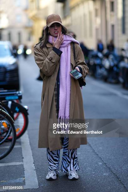 Guest wears a brown suede cap, gold earrings, a pale purple wool fringed scarf, a brown oversized long coat, a black shiny leather shoulder bag,...