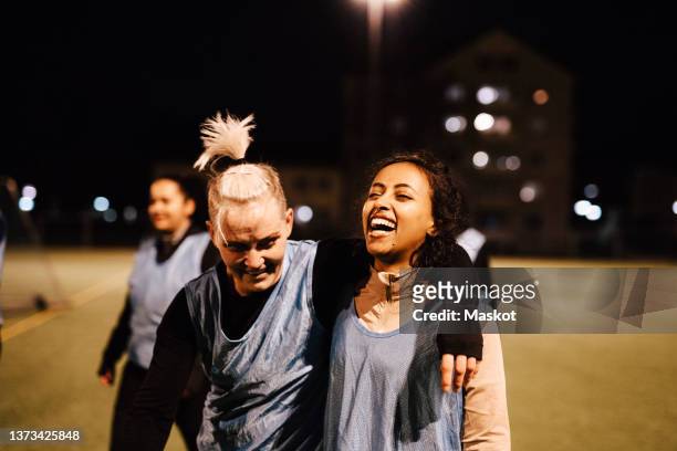 sportswoman with arm around cheerful female athlete walking on field at night - woman football stock-fotos und bilder