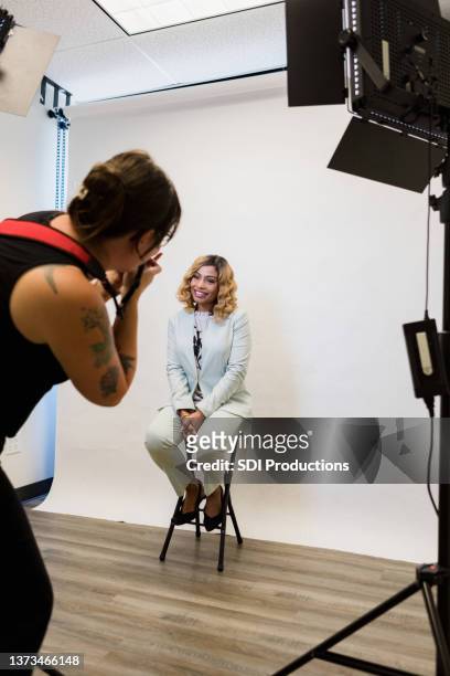 businesswoman sitting on stool smiles for publicity photo - photo shoot stockfoto's en -beelden