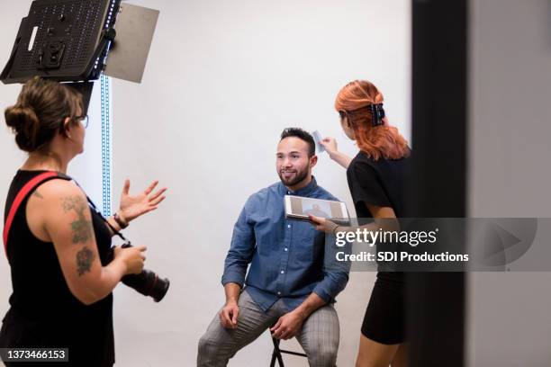 female assistant helps female photographer prepare businessman for photoshoot - backstage photography stock pictures, royalty-free photos & images