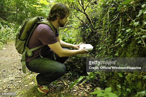 Man holding a geocache on the side of a path in a forest while geocaching on July 5 Monkton Farleigh.